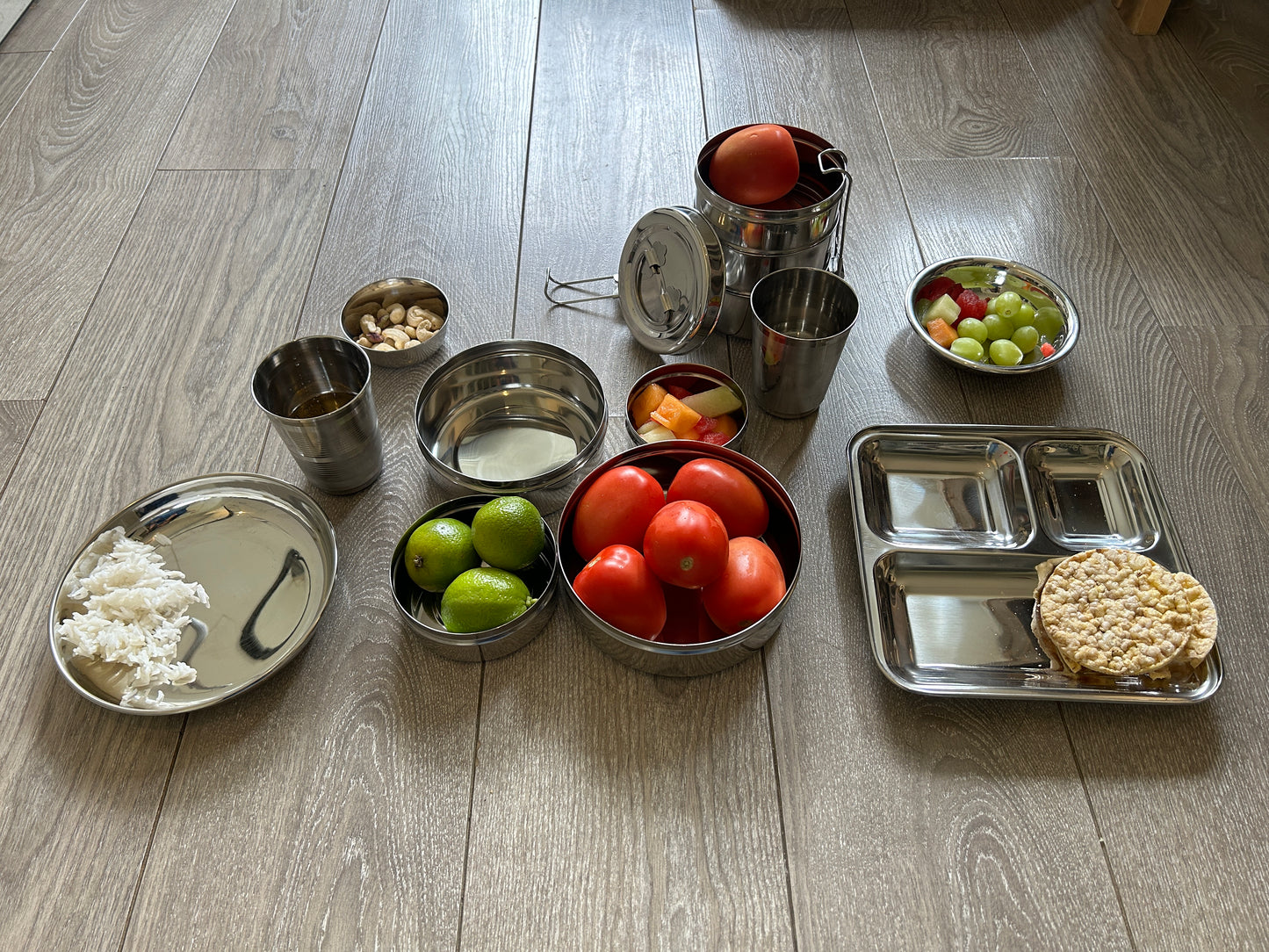 Collection of stainless steel containers with food items on a wooden floor