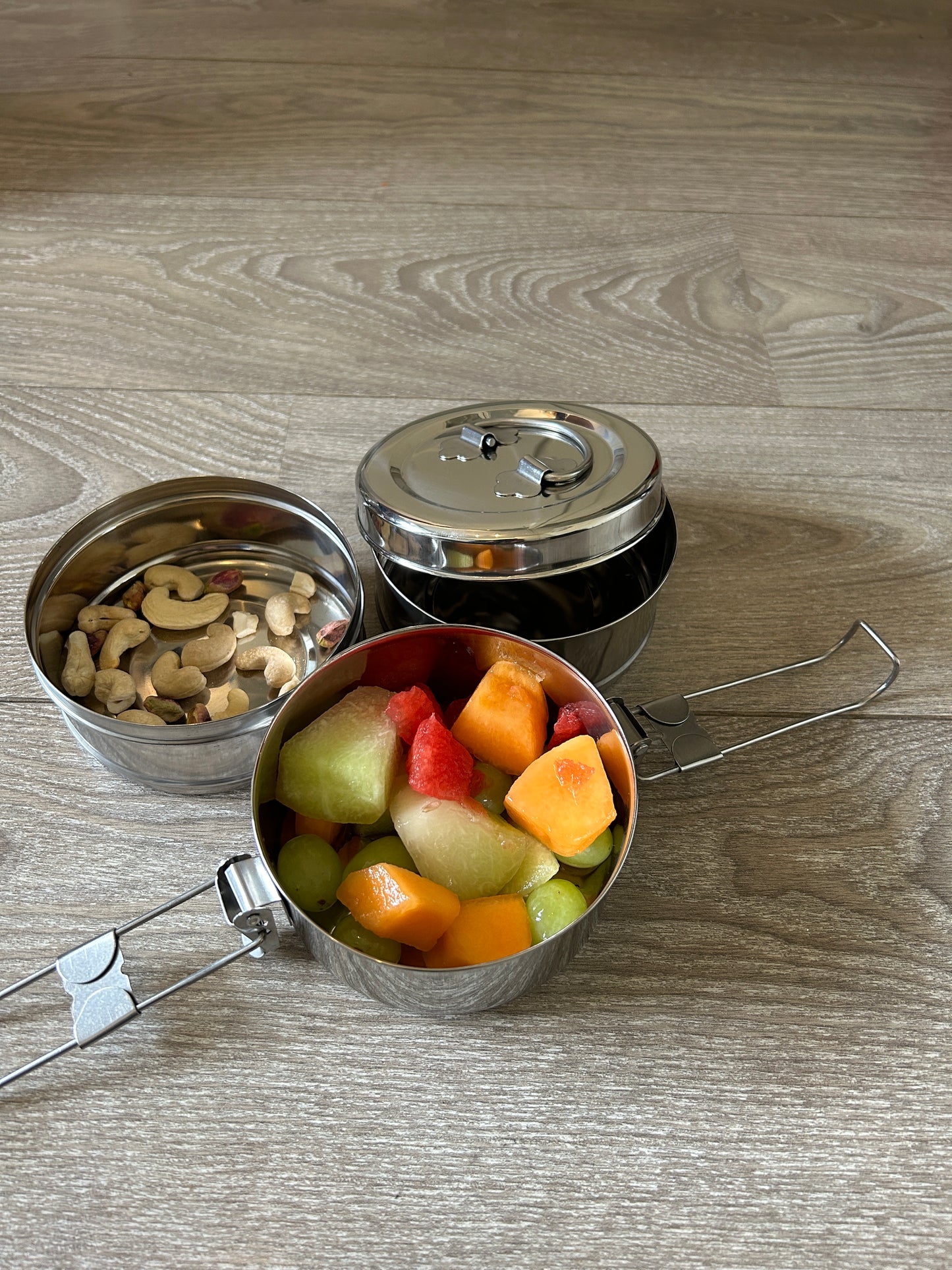 Metal snack container with fruits and nuts on a wooden surface