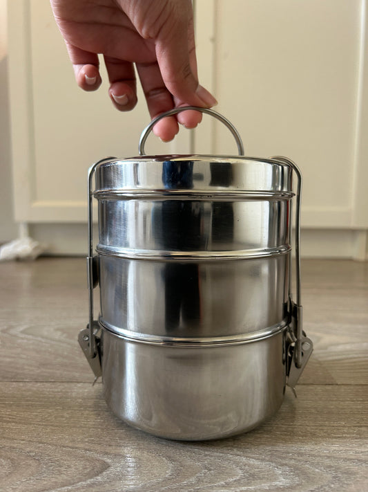 Metallic canister held by a hand against a neutral background